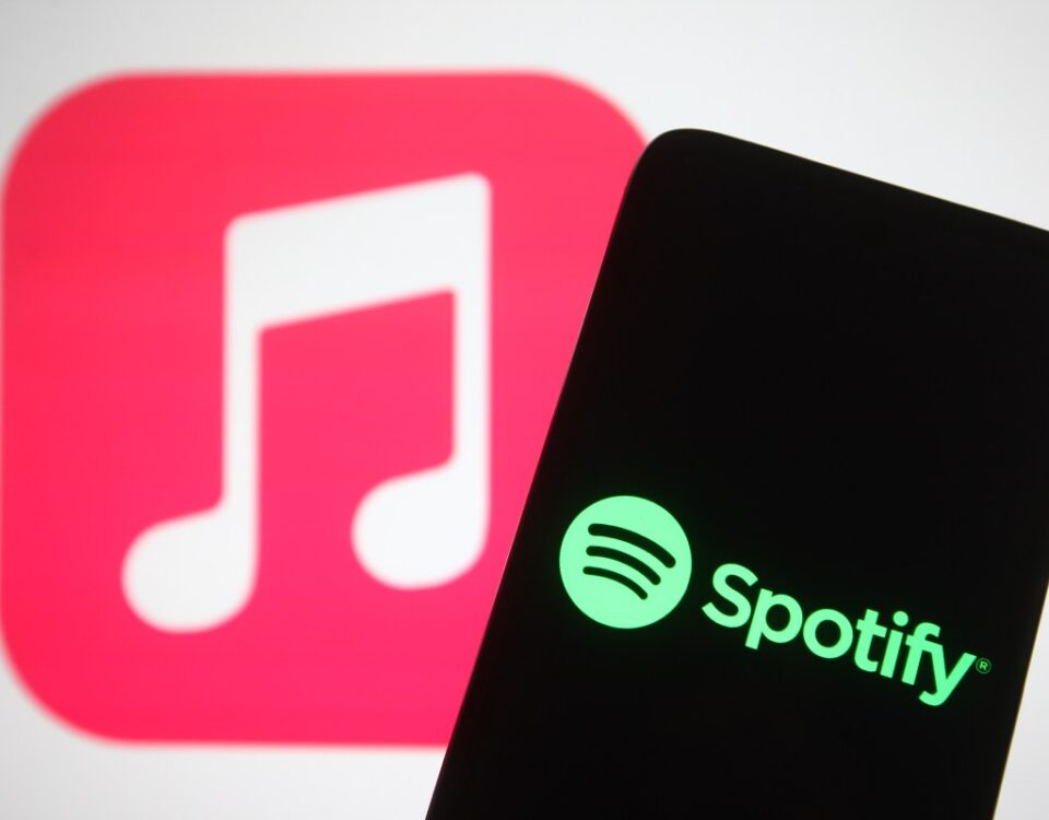 The Spotify logo seen displayed on a smartphone screen in front of Apple Music logo in the background.