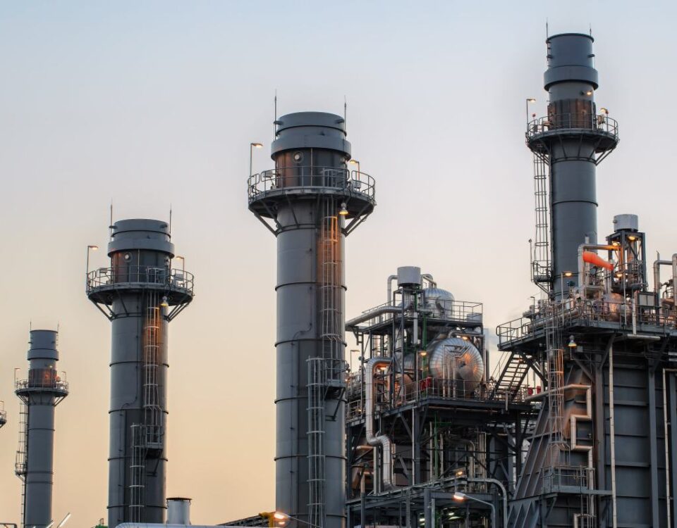 Natural gas power plant smoke stacks stand against a twilight sky.