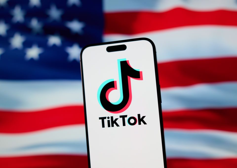 The TikTok app and logo are seen on a mobile device in front of a US flag