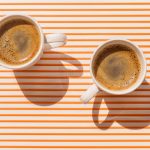 Two white coffee cup on orange striped table at direct sunlight. Top view with shadow.