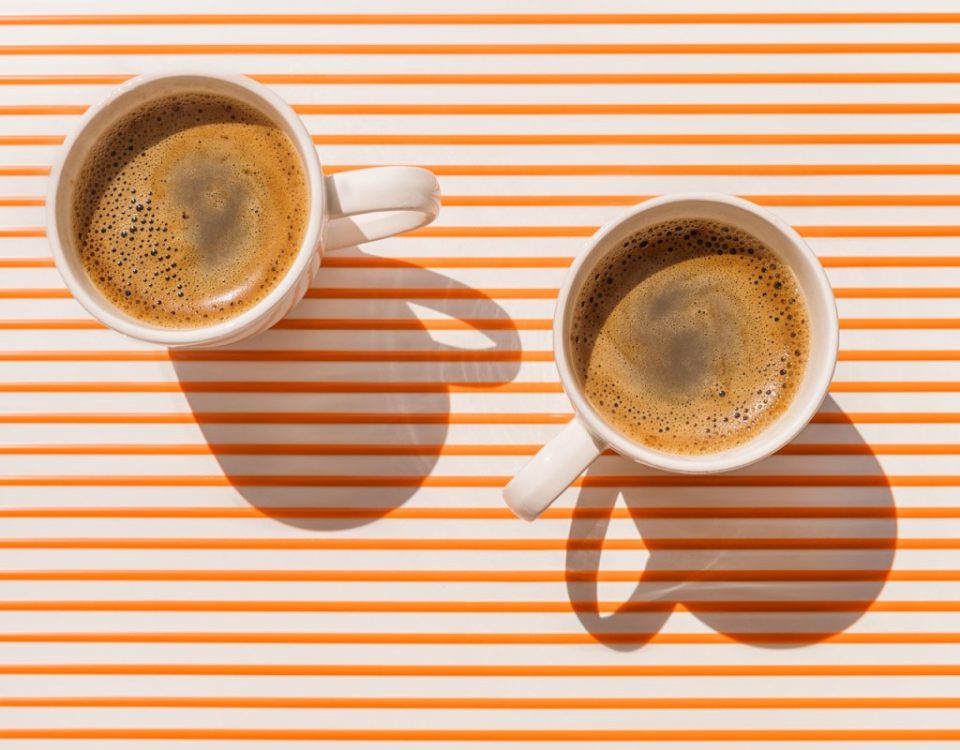 Two white coffee cup on orange striped table at direct sunlight. Top view with shadow.