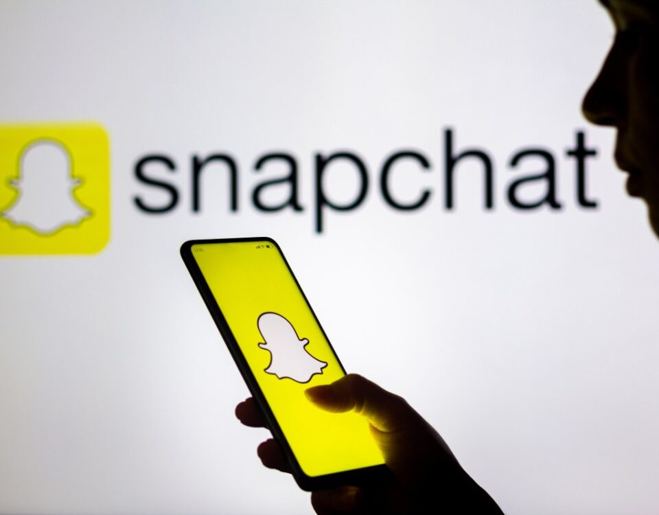 In this photo illustration, a woman's silhouette holds a smartphone with the Snapchat logo displayed on the screen and in the background.