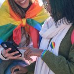 Two young women are using a smartphone while showing their support for LGBTQ+ rights
