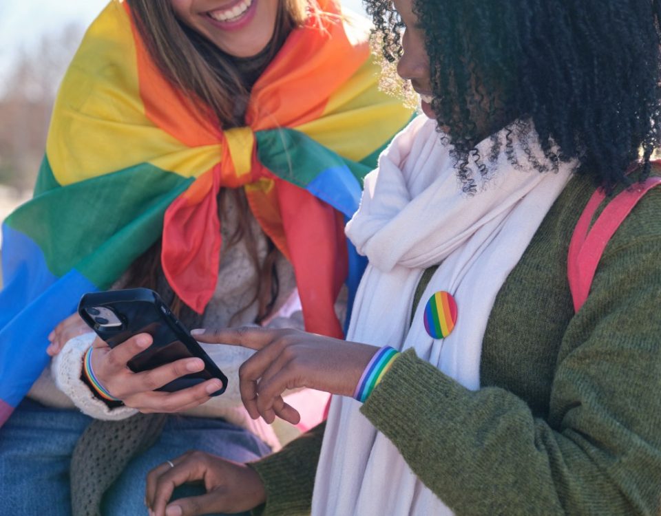 Two young women are using a smartphone while showing their support for LGBTQ+ rights