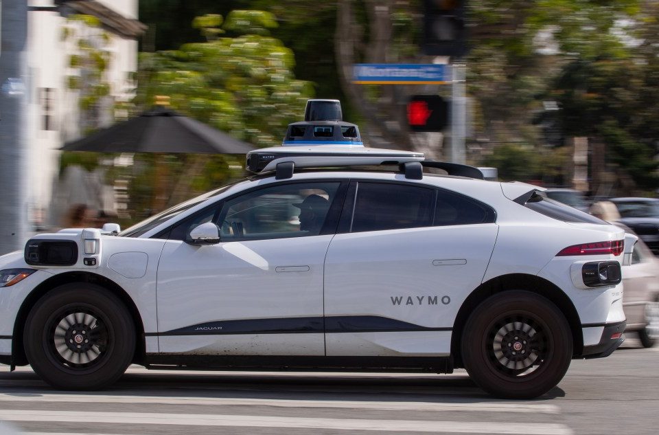 A Waymo autonomous vehicle operating on a tree-lined street in Santa Monica.