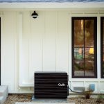 A Quilt heat pump outdoor unit sits outside a white house.