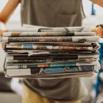 A person holding a pile of newspapers.