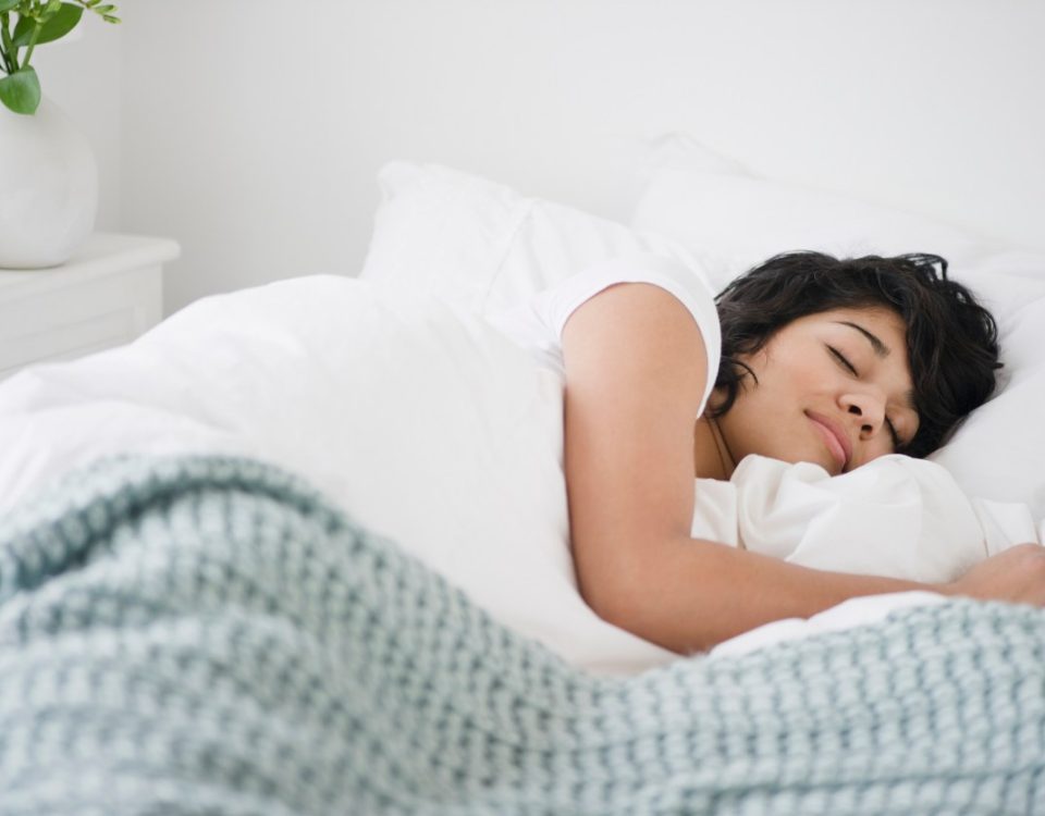 Photo of a woman sleeping in a bed with white pillows and a blue blanket