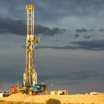A rig drills into the earth against a cloudy sky.