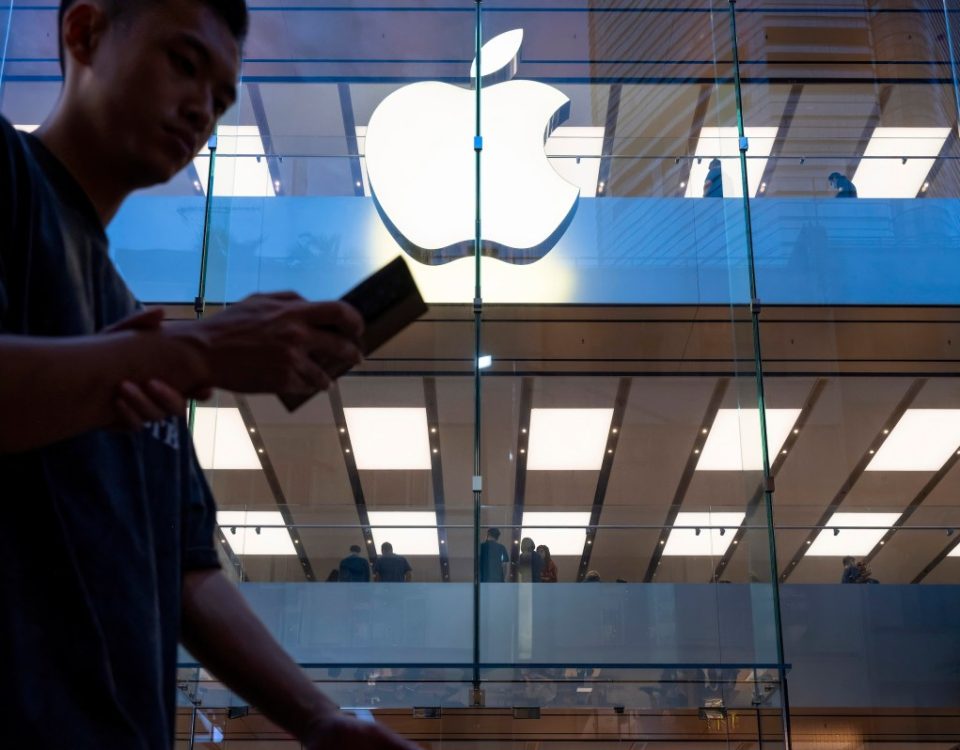 A pedestrian uses a smartphone while walking past an Apple store and logo in Hong Kong.