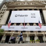 A mail carrier wearing a protective mask passes a banner displaying Palantir Technologies Inc. signage during the company's initial public offering (IPO) in front of the New York Stock Exchange (NYSE) in New York, U.S., on Wednesday, Sept. 30, 2020.