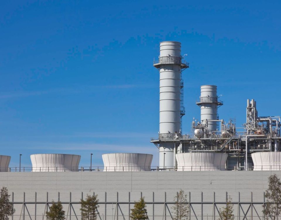 Smoke stacks from a natural gas power plant stand against a blue sky.