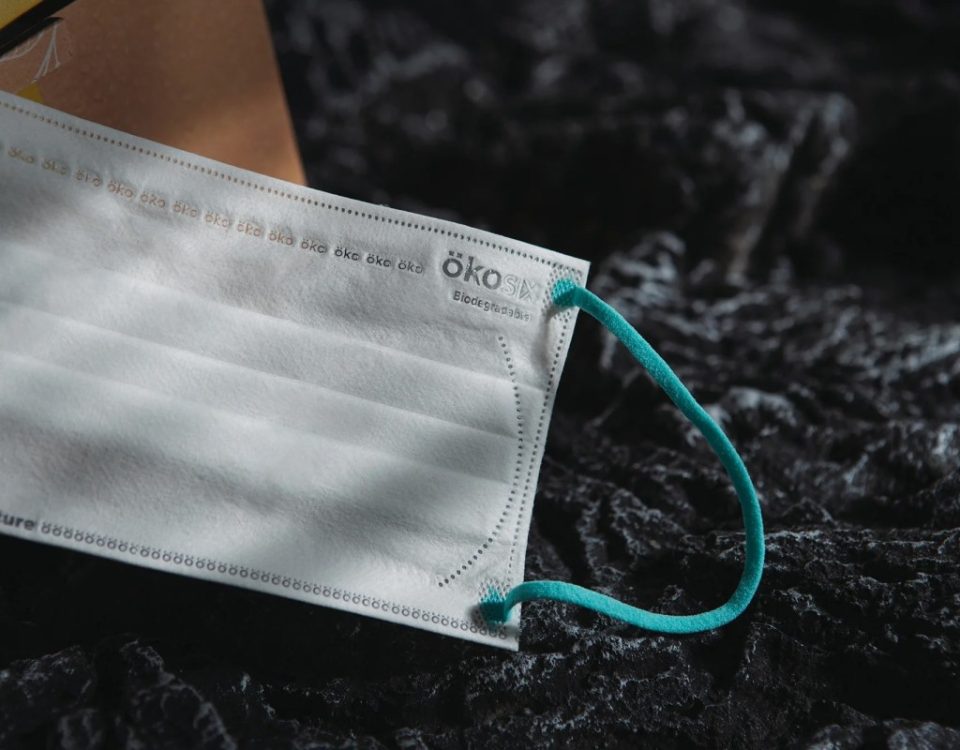 A white surgical mask sits on a black rock.