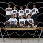 Eight people stand and sit on a thin panel of wood to demonstrate its strength.