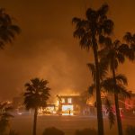 A firefighter watches the flames from the Palisades Fire burning homes on the Pacific Coast Highway amid a powerful windstorm on January 8, 2025 in Los Angeles, California.