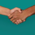 Handshake of Black and white teens shaking hands, against blue background, closeup