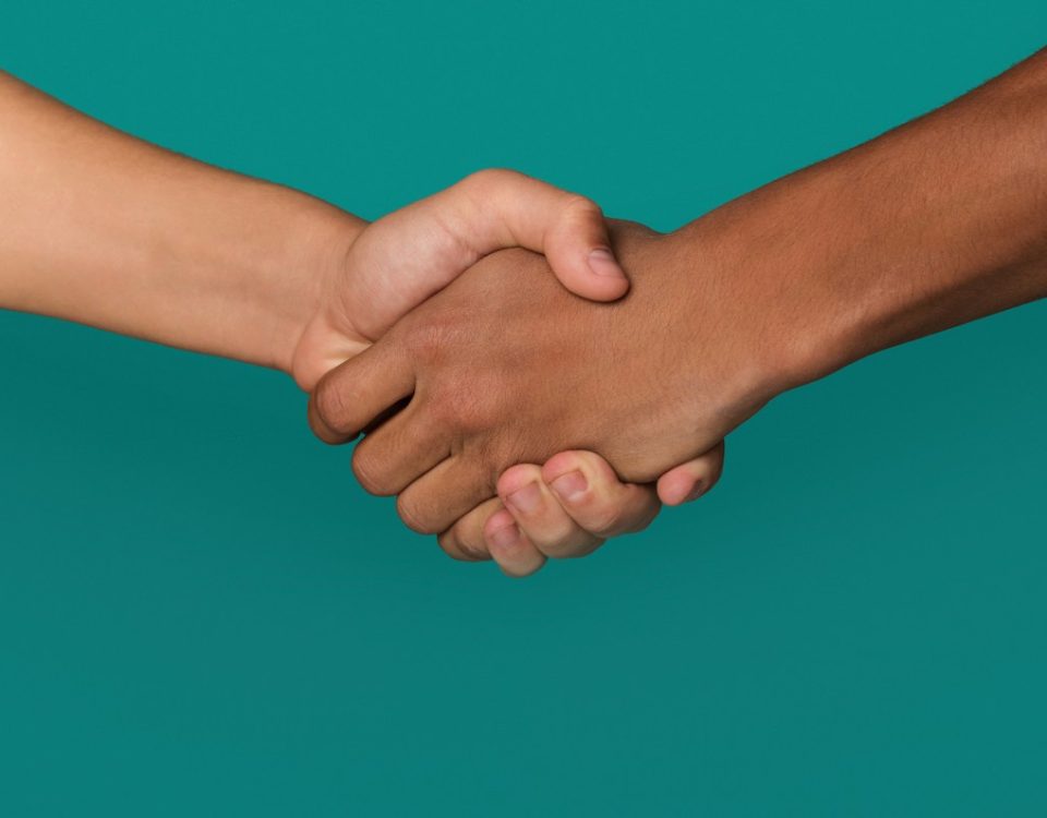 Handshake of Black and white teens shaking hands, against blue background, closeup
