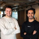 Two men stand with folded arms in a corporate office.