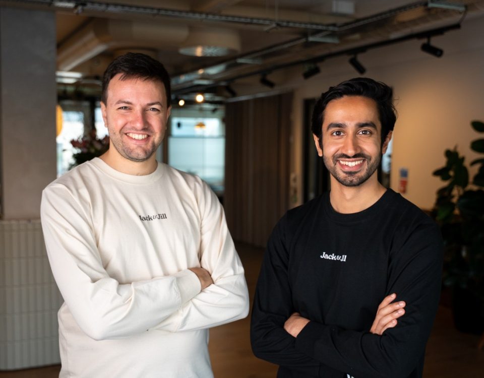 Two men stand with folded arms in a corporate office.