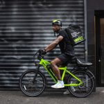 Side shot of food delivery worker on Whizz e-bike on NYC street in front of street mural