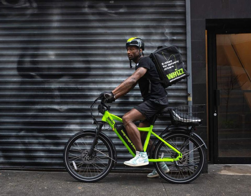 Side shot of food delivery worker on Whizz e-bike on NYC street in front of street mural