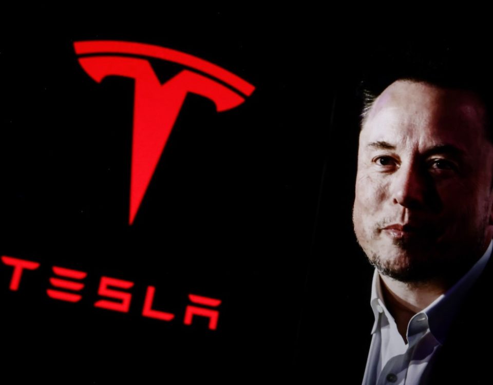 Elon Musk next to large red Tesla logo