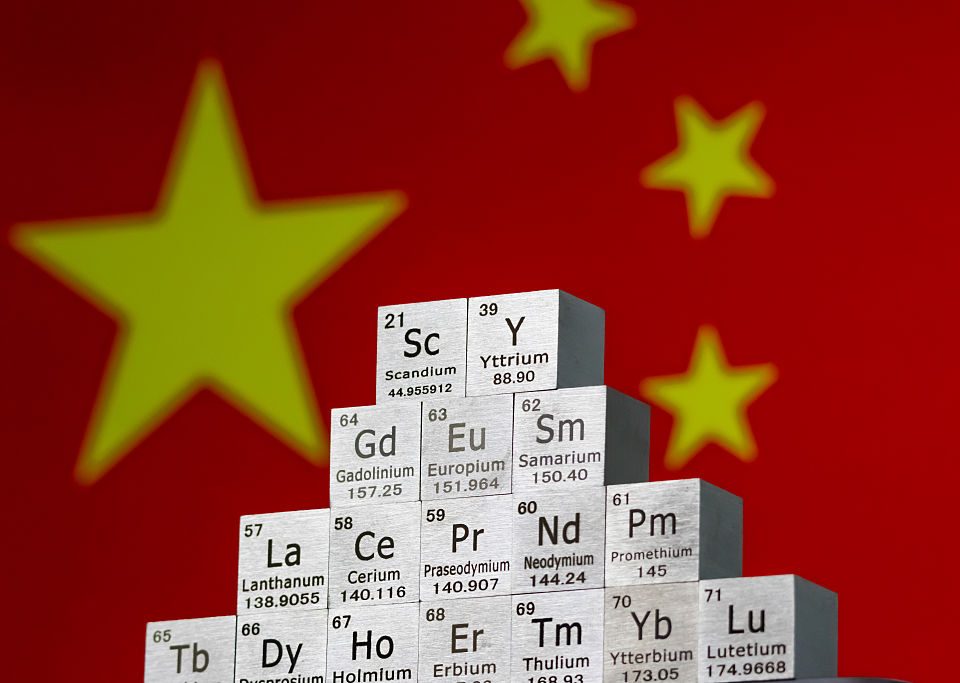 In this photo illustration, metal cubes representing rare earth elements including Scandium (Sc), Yttrium (Y), Neodymium (Nd), Lanthanum (La), and others are stacked in a stepped formation in front of the national flag of China